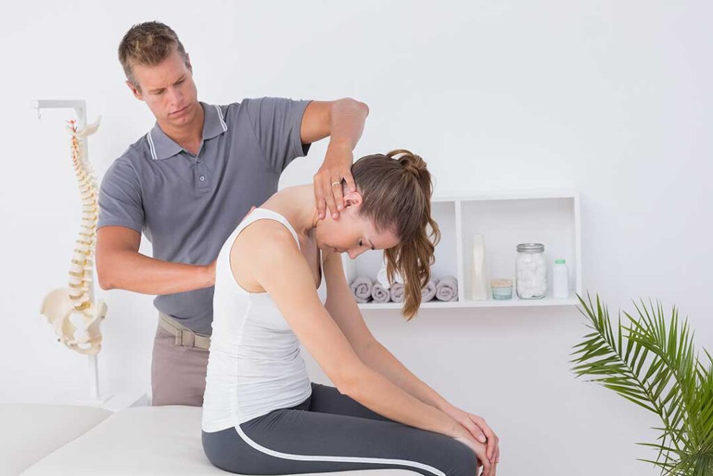 Person adjusting a monitor while seated upright with relaxed shoulders and feet supported.